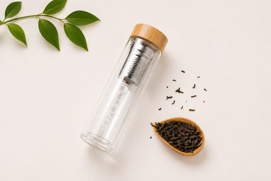 Transparante glazen theefles met bamboe dop en roestvrijstalen thee-infuser op een schone neutrale achtergrond, minimalistische productfoto voor Shopify-webshop.